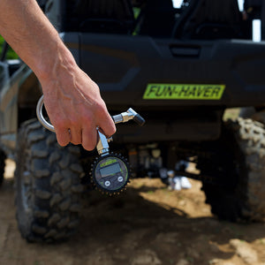 A hand holding the Fun-Haver digital tire gauge with a UTV in the background