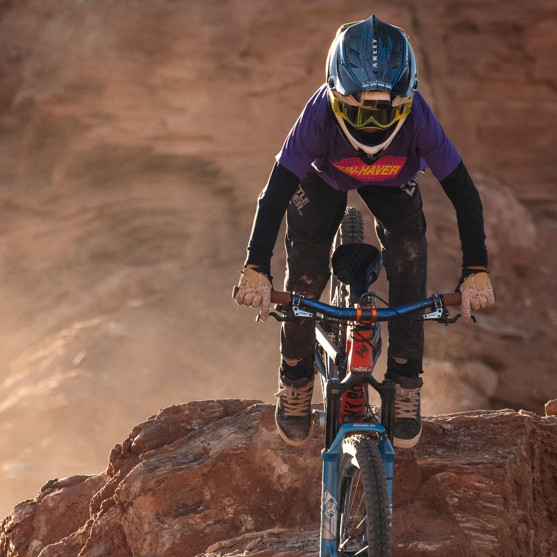 Future lifelong Fun-Haver wearing the Fun-Haver Purple Rush Pursuit Youth T-Shirt with Magenta and Yellow Fun-Haver logo graphics in 2 wheel action on the rocks
