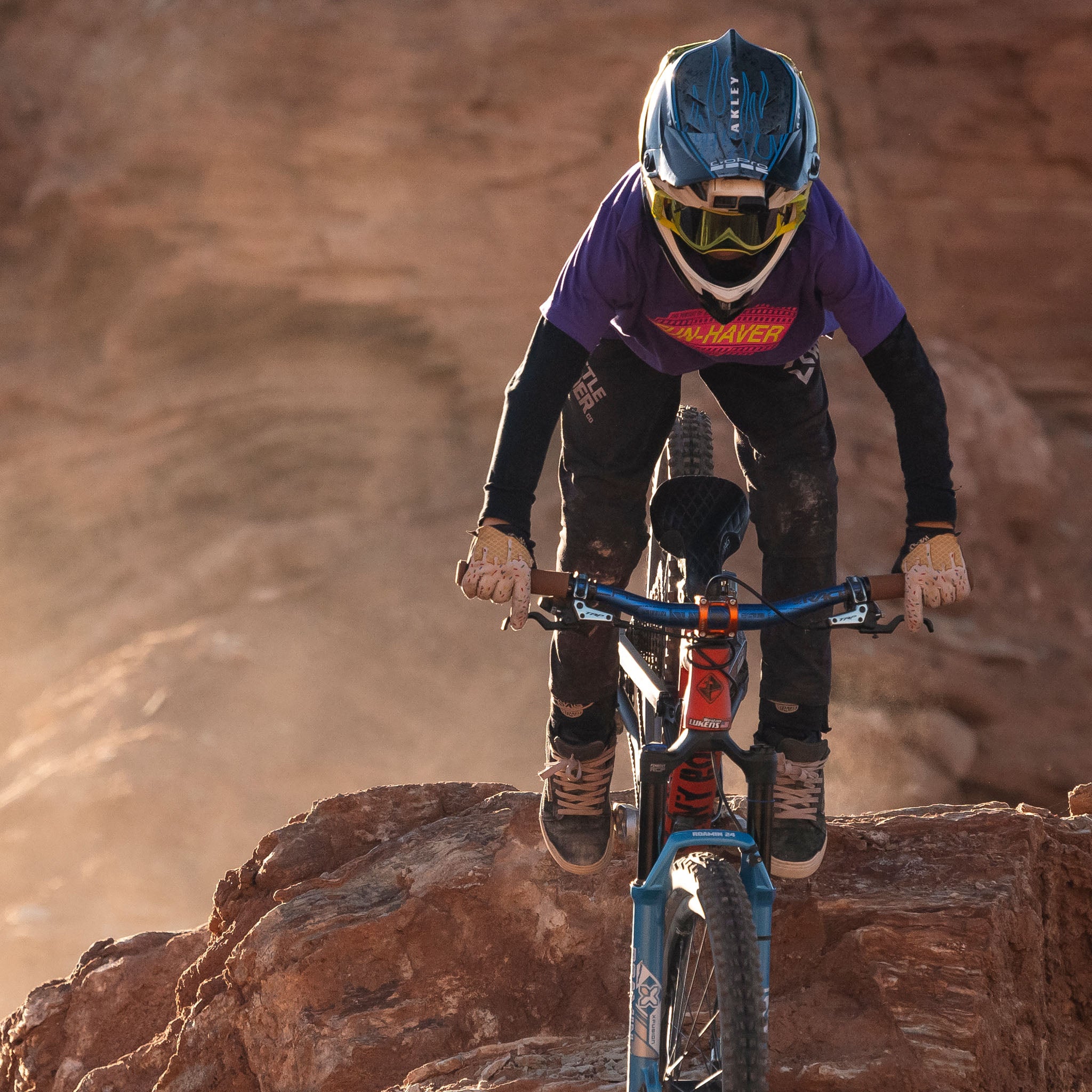 Future lifelong Fun-Haver wearing the Fun-Haver Purple Rush Pursuit Youth T-Shirt with Magenta and Yellow Fun-Haver logo graphics in 2 wheel action on the rocks