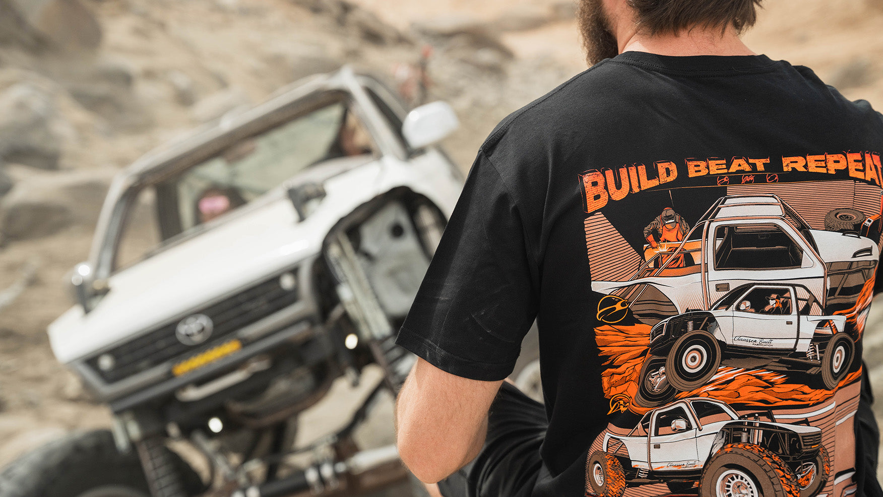 A closeup photo of a man on an off-road truck trail in front of a modified off-road truck