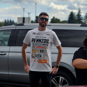 Man in a white t-shirt standing next to a car with a colorful design on a cloudy day.