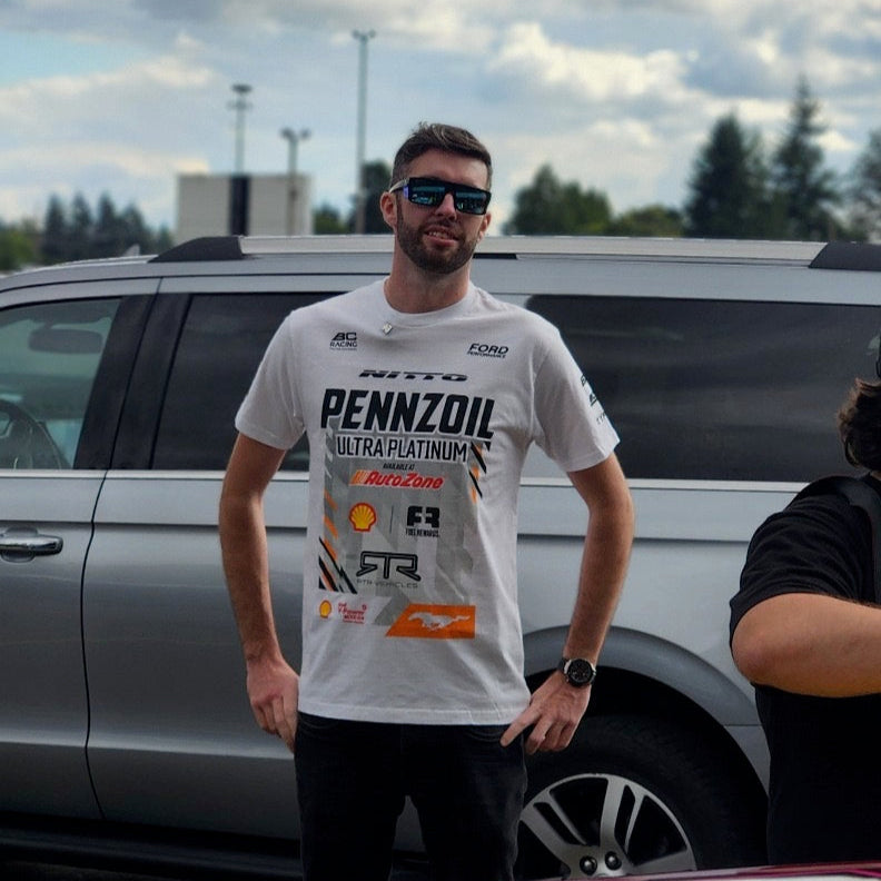 Man in a white t-shirt standing next to a car with a colorful design on a cloudy day.
