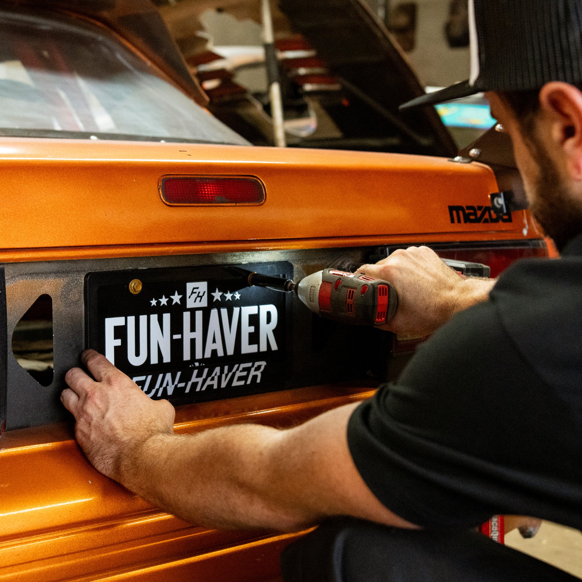 Fun-Haver Blaize Potts installing the Full Time Fun-Haver metal license plate on his Orange Mazda RX-7 FC.