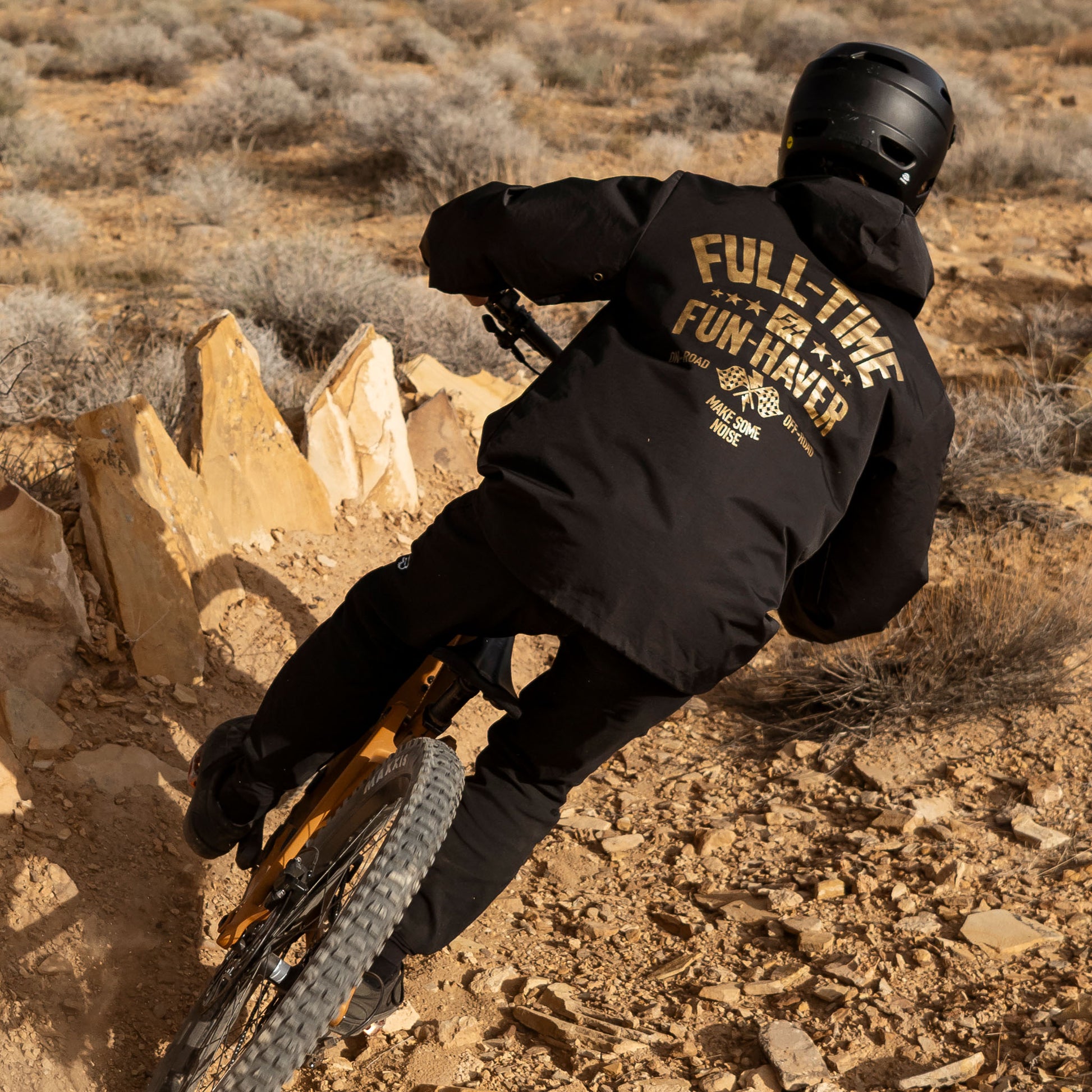 Back view of Joel riding his mountain bike while wearing the Black Full Time Fun-Haver® Winbreaker Coaches Jacket.